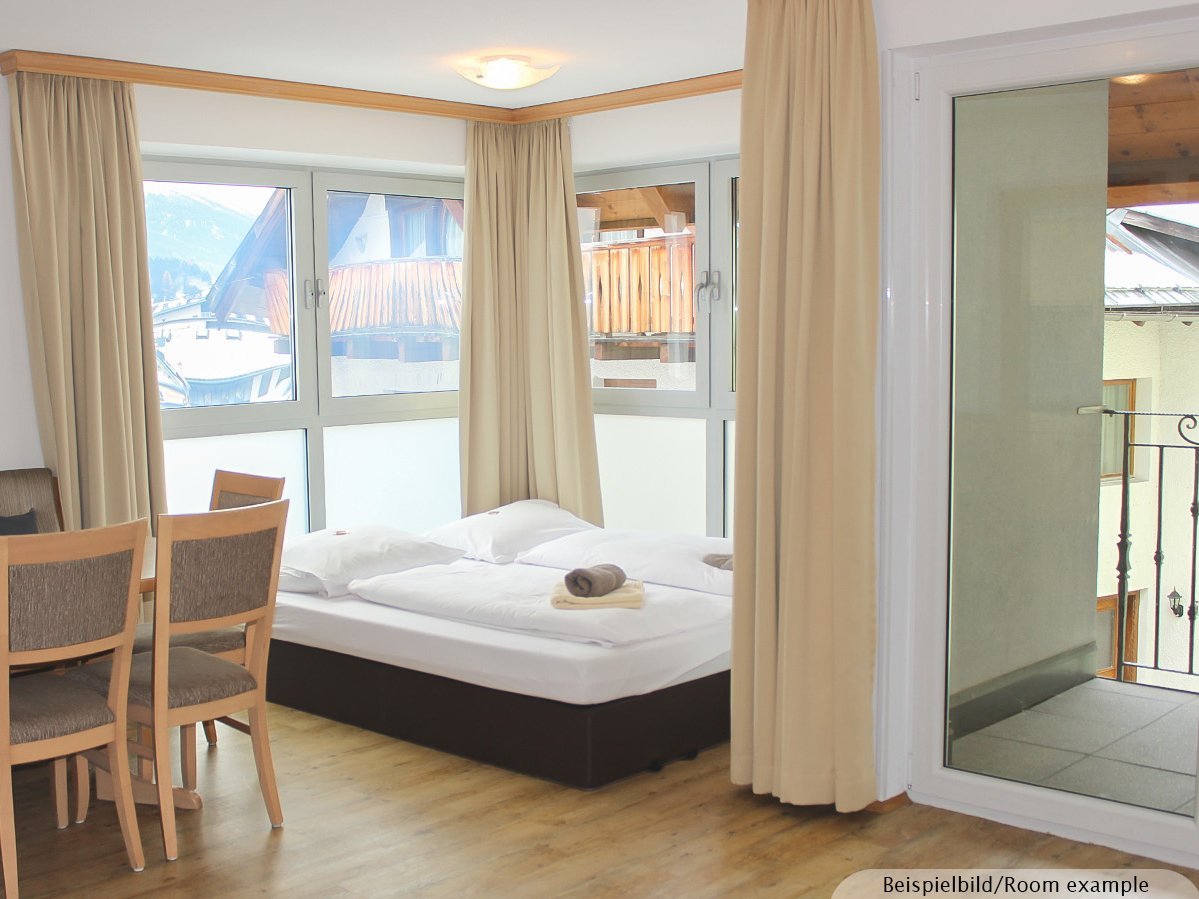 Bild zeigt einen Wohnraum mit einem aufgebetteten Schlafsofa, einer Sitzgruppe und einen Zugang zu einem Balkon